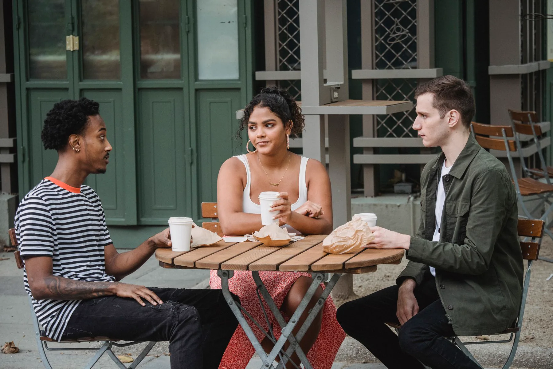 Three friends talk over coffee at an outdoor cafe.