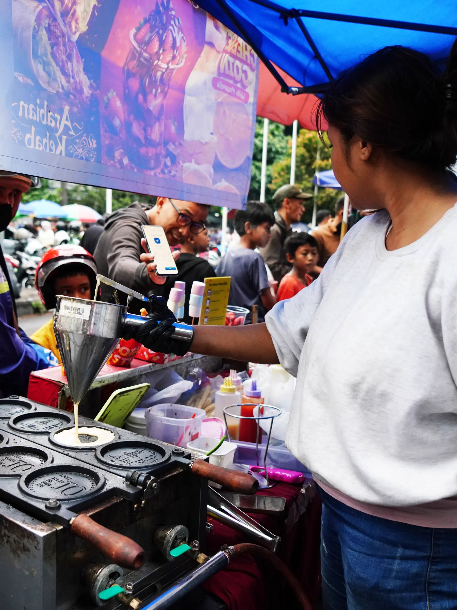 A street-food vendor serves a customer at a busy market.