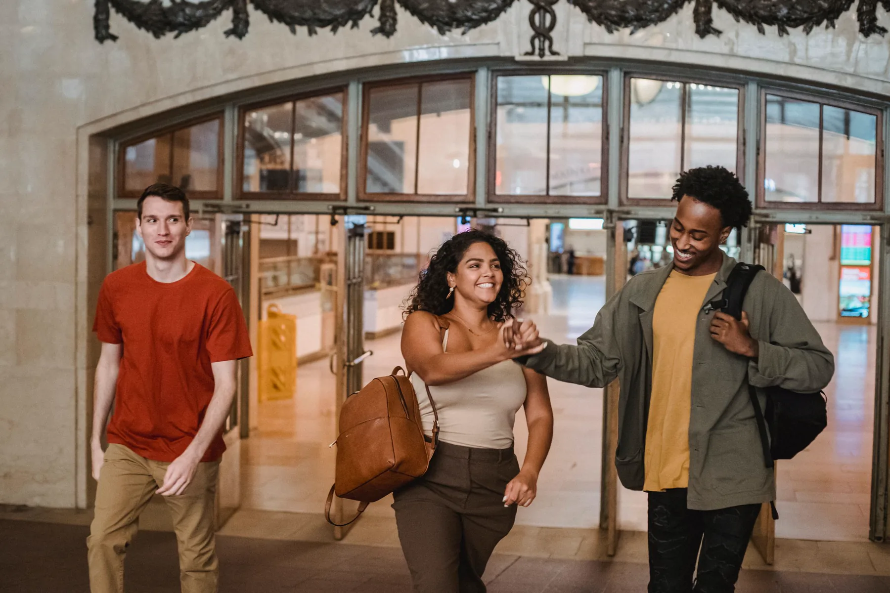 Three young adults greet one another while walking through a university building.
